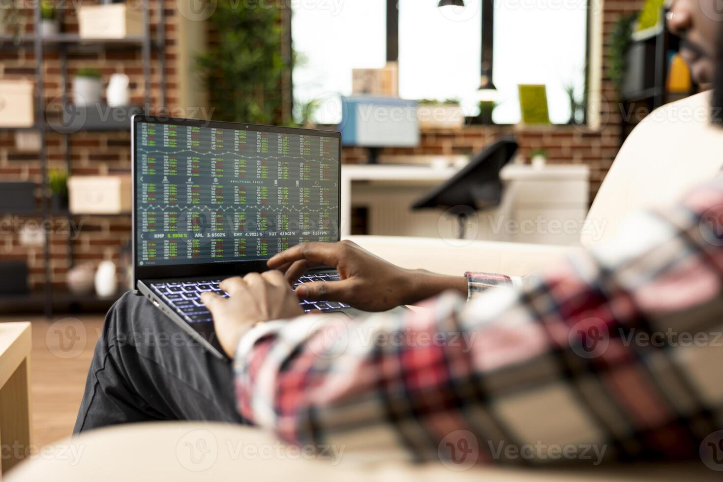 An African American investor studying financial charts and market data on a laptop